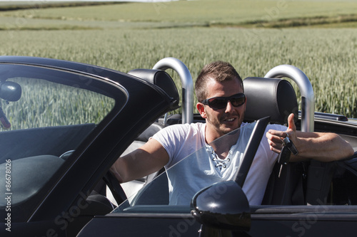 Mann mit Sonnenbrille sitzt im Auto mit dem Schlüssel