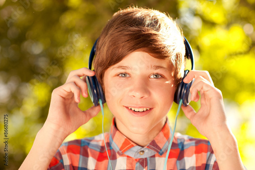 Kid boy listen to music outdoors. Looking at camera. 