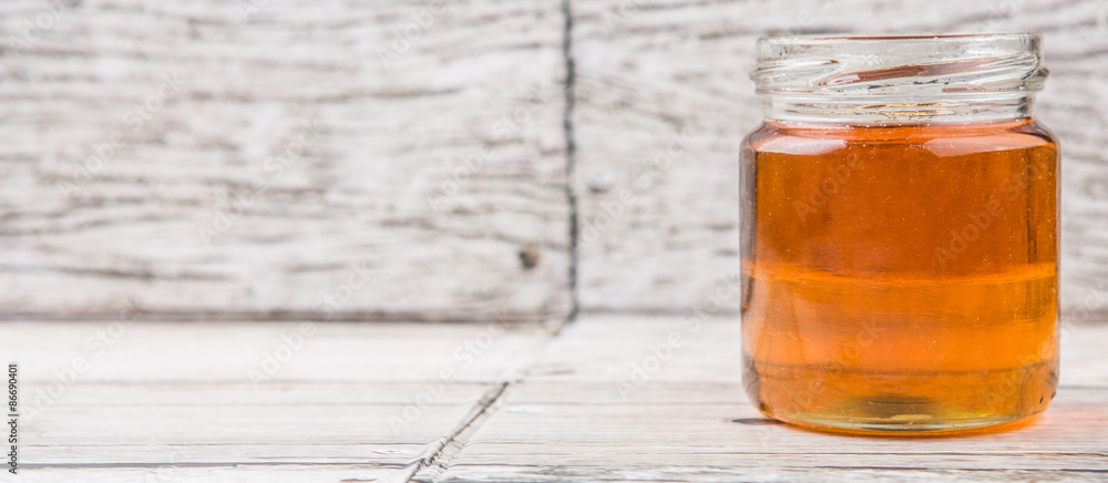 Honey in a mason jar over rustic weathered wooden background Honey in a mason jar over rustic weathered wooden background