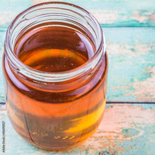 Honey in a mason jar over rustic weathered wooden background