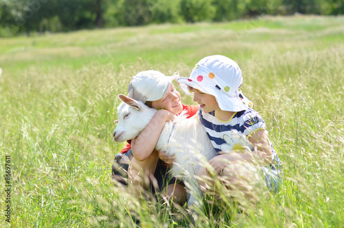Brother and sister hugging baby goat in the field