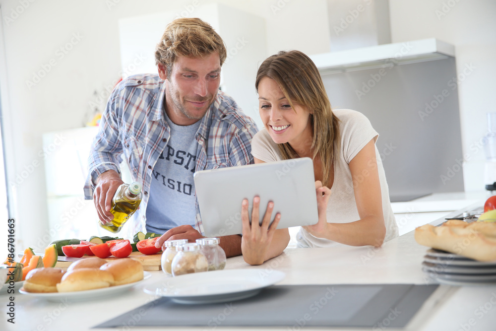 Cheerful couple in kitchen cooking dinner, using tablet Cheerful couple in kitchen cooking dinner, using tablet