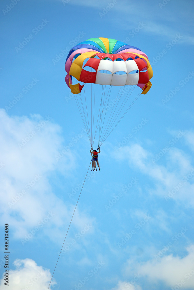 Two people parasailing with parachute on blue sky with clouds Two people parasailing with parachute on blue sky with clouds