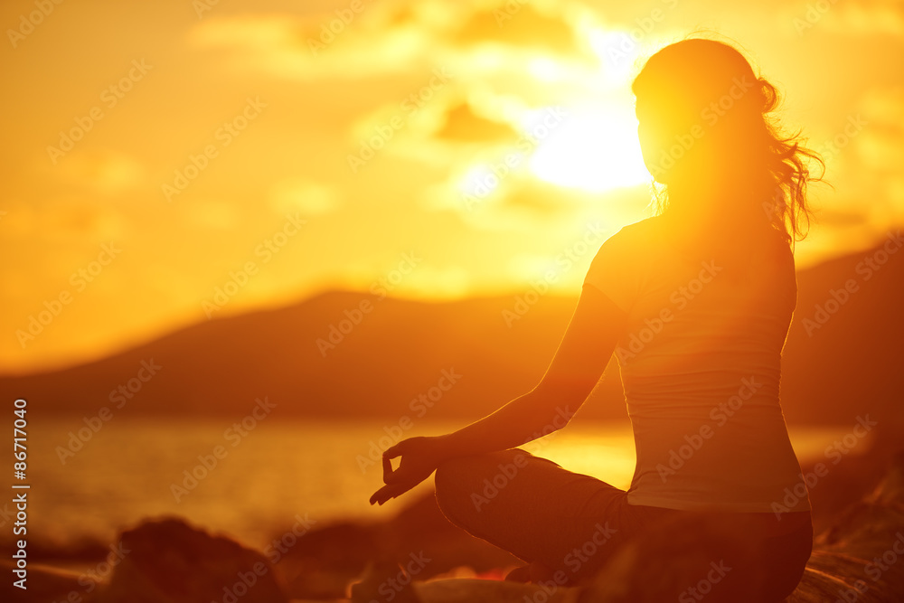 woman meditating in lotus pose on the beach at sunset woman meditating in lotus pose on the beach at sunset