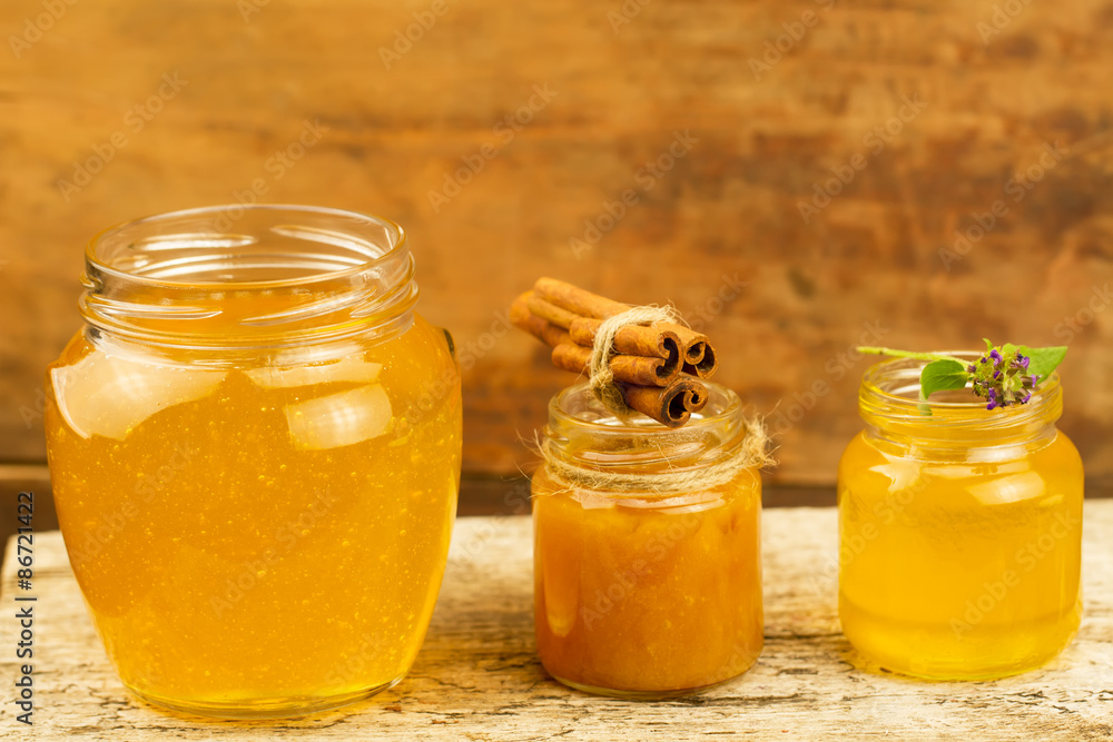 three jars of honey with cinnamon, flowers on wooden background three jars of honey with cinnamon, flowers on wooden background
