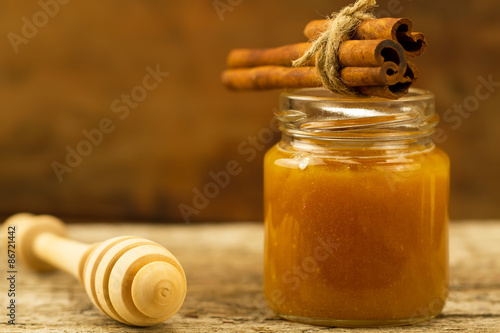 small jar of honey with drizzler and cinnamon on wooden background
