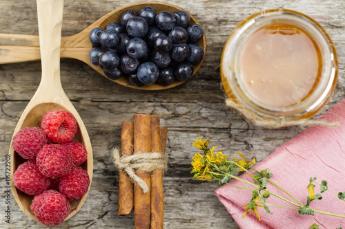 Fototapeta Naklejka Na Ścianę i Meble -  Raspberries and blueberries in spoons with pink napkin and a jar of honey with cinnamon on wooden background. Healthy eating, diet