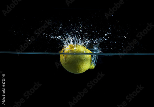 Limone cade in acqua producendo schizzi ed onde. Luce radente blu e sfondo nero