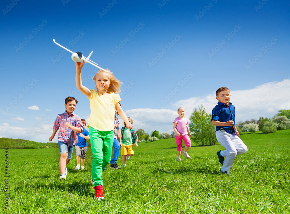 Small girl runs with kids and holds airplane toy Small girl runs with kids and holds airplane toy