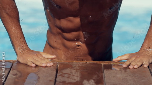 Wet sexy man with six-pack climbs out from the private pool on