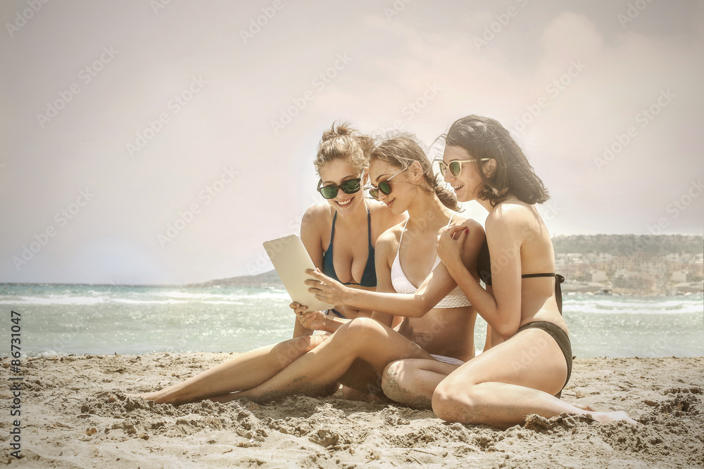Fototapeta premium Three girls at the beach staring at a tablet