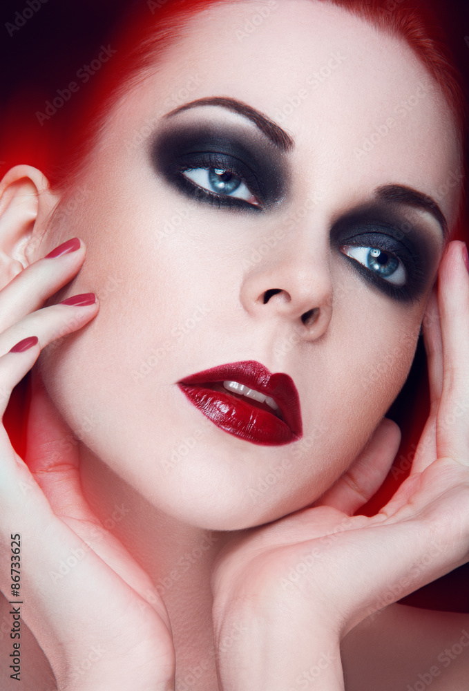 Beauty portrait of young women with blue eyes, red lipstick, smoky eyes, hand touching face on black background. Beauty portrait of young women with blue eyes, red lipstick, smoky eyes, hand touching face on black background.