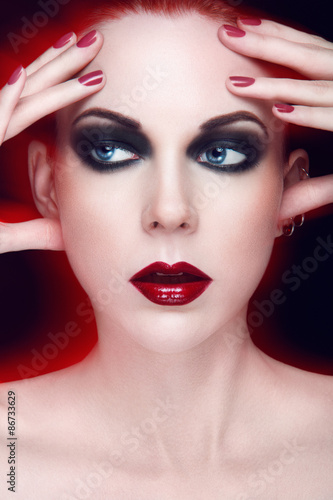 Beauty portrait of young women with blue eyes  red lipstick  smoky eyes  hand touching face on black background.