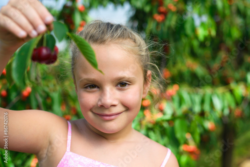 Closeup portrait smiling girl holding cherry in cherry garden
