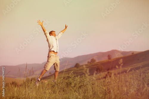 Guy with Outstreched arms jump in a green grass meadow in a mountain