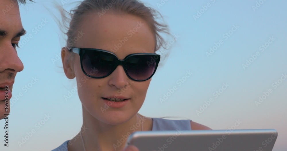 Young people looking at sunset and using pad Young people looking at sunset and using pad