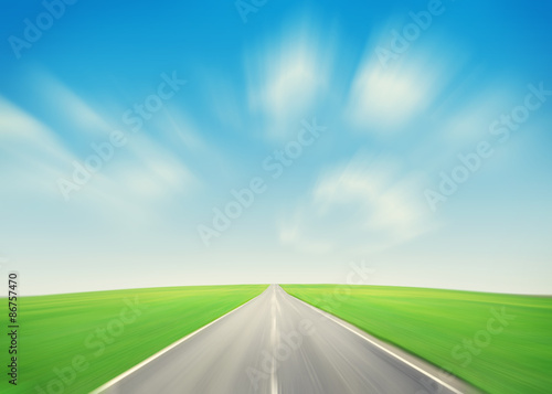 Asphalt road through the green field and blue sky