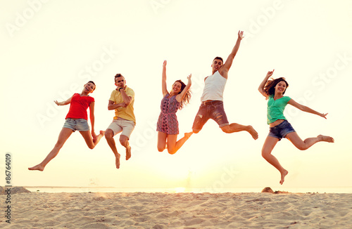 smiling friends dancing and jumping on beach