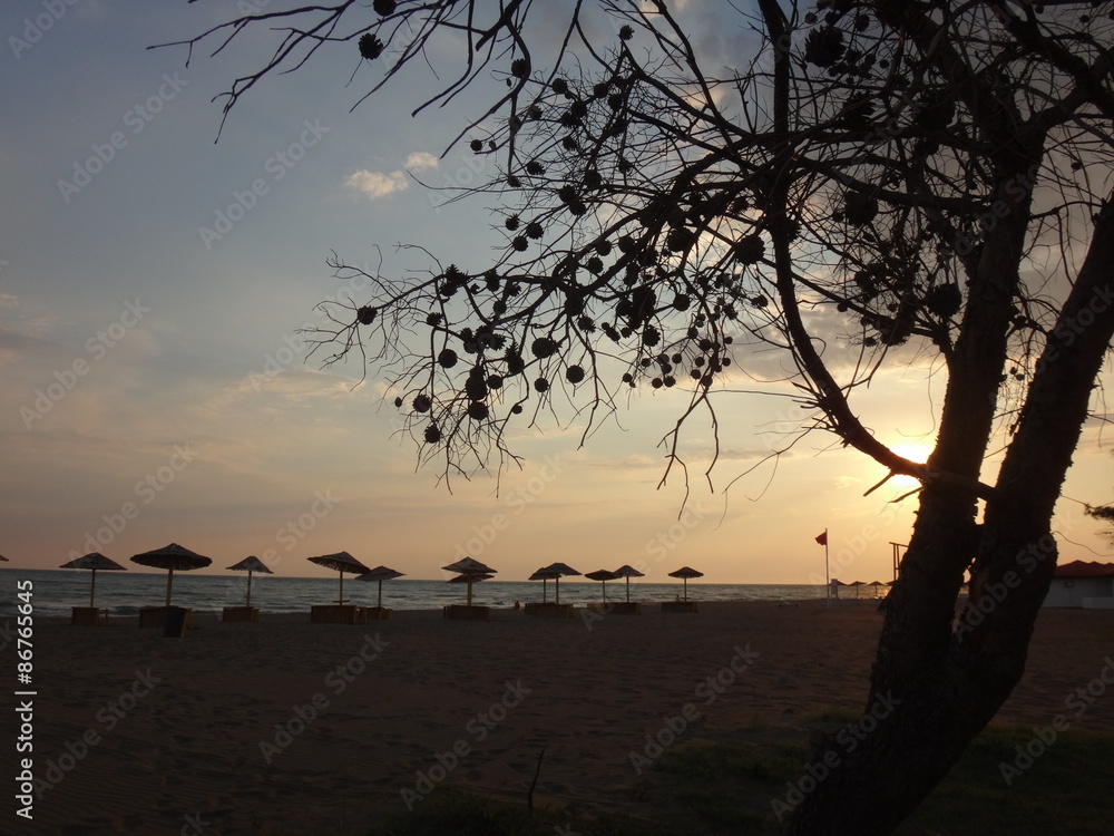 Закат над песчаным морским пляжем и зонтики на его фоне