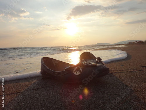 Закат над песчаным морским пляжем и женские туфли, оставшиеся на песке