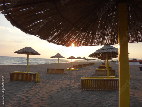 Закат над песчаным морским пляжем и зонтики на его фоне