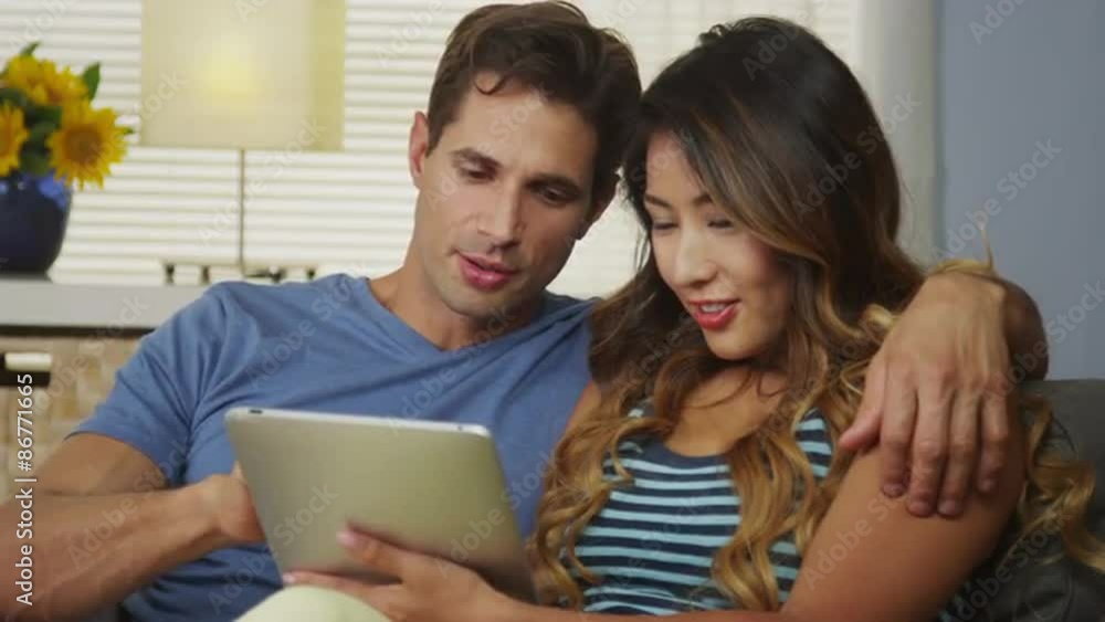 Happy interracial couple using tablet together on couch Happy interracial couple using tablet together on couch