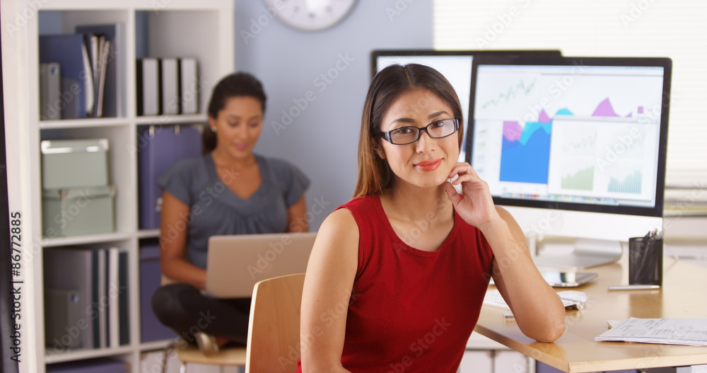 Japanese businesswoman sitting at desk with colleague in Mexican background