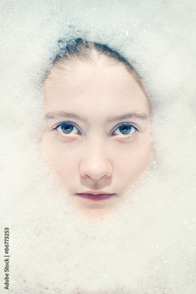 Beautiful girl face in bubble bath with fluffy white foam around