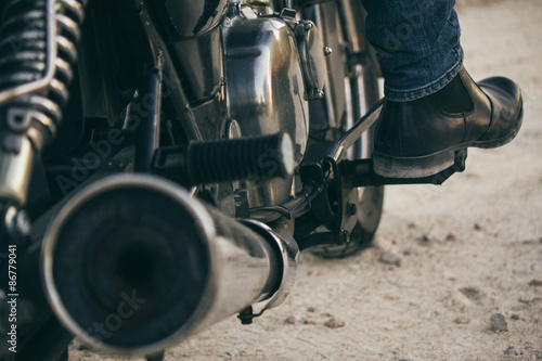 Foot of a man sitting on his motorbike on a dirt road