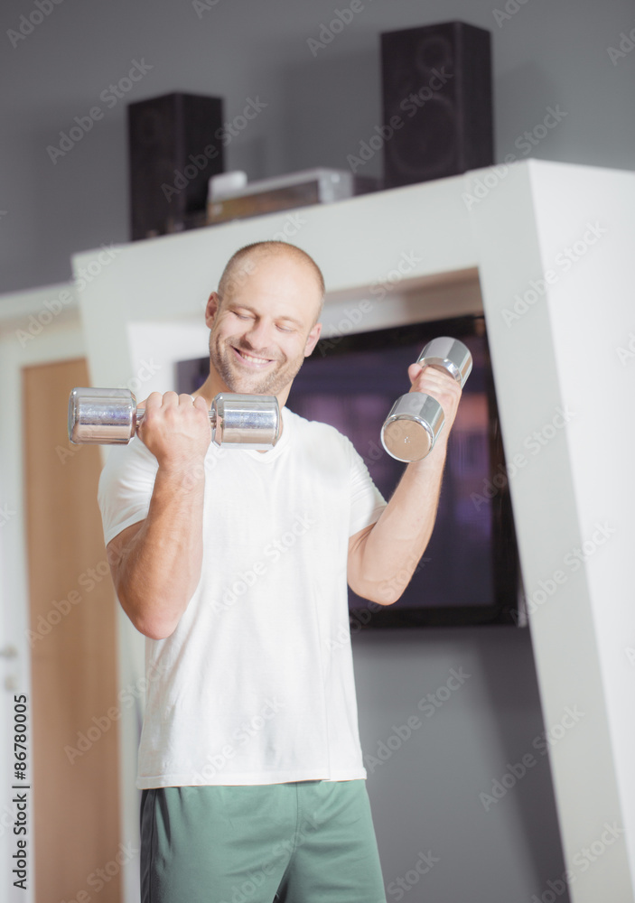 Satisfied young strength man lifting dumbbell at home