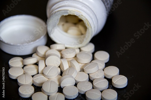 Fotografie Round White tablets (medcine or food suplier) out of bottle on black background