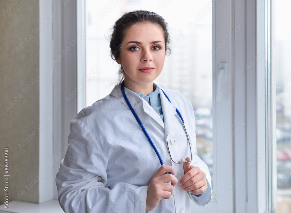 Portrait of young woman doctor on white coat standing near window Portrait of young woman doctor on white coat standing near window