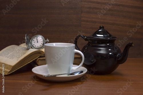 Tea cups with teapot, books and old pocket watch on wooden table