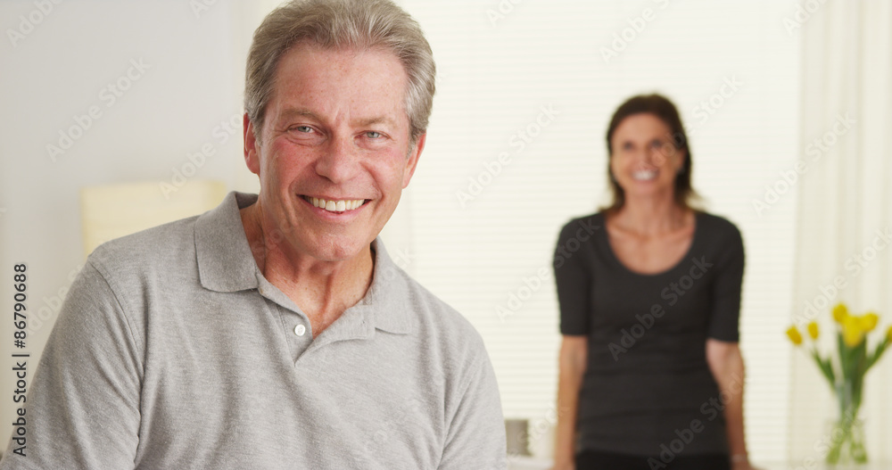Happy Elderly couple standing in living room looking at camera Happy Elderly couple standing in living room looking at camera