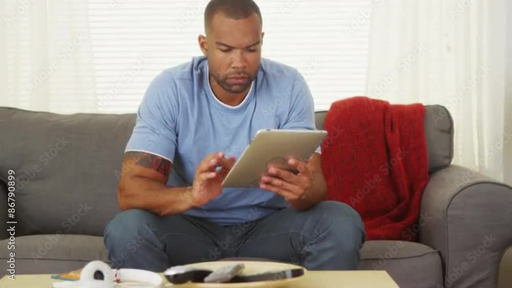 Black man sitting on couch using tablet