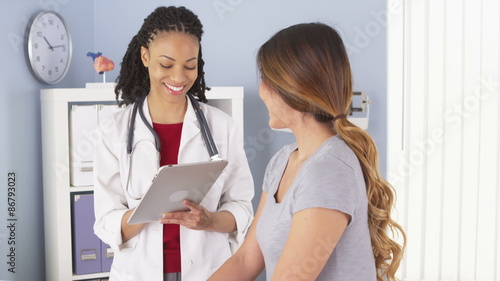Black doctor with tablet talking to female Asian patient