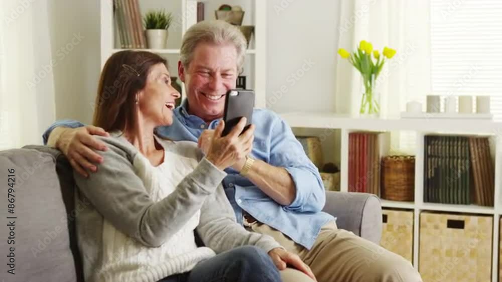 Senior couple using smartphone on couch Senior couple using smartphone on couch