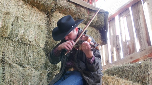 Cowboy plays old fiddle in his barn on the haystack photo