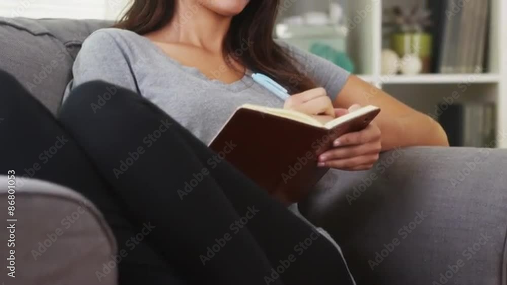 Mixed race woman sitting on couch writing in journal Mixed race woman sitting on couch writing in journal