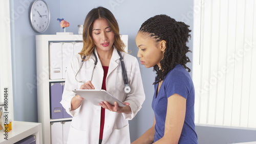 African American patient explaining issues to Asian doctor using tablet