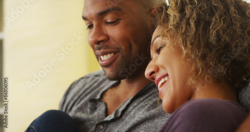 Black couple sitting on couch smiling © rocketclips