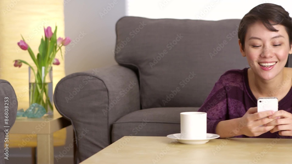 Happy Chinese woman texting on smartphone at home Happy Chinese woman texting on smartphone at home