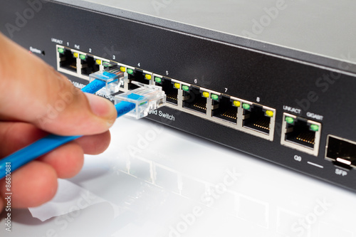 LAN network switch with ethernet cables plugging in on white