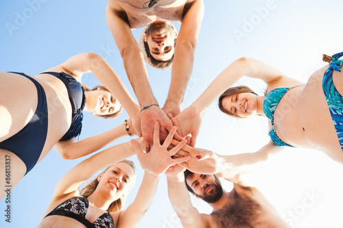 Group of friends in a swimsuit on the beach with hands collected one above the other in trip to the beach. Bottom view in the evening, with the sun low behind them