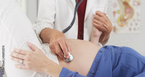 Senior doctor listening to pregnant woman's stomach