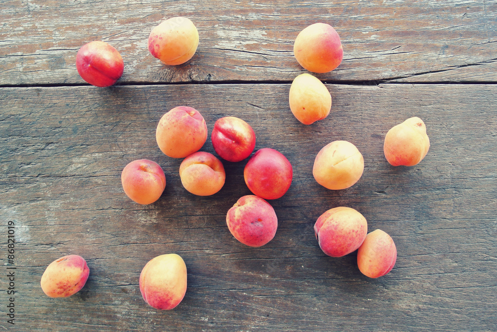 Obraz premium Ripe fresh orange apricots scattered on the rustic wooden table. Image edited in faded, washed out, nostalgic, retro style; rural vintage concept. Organic farming concept.