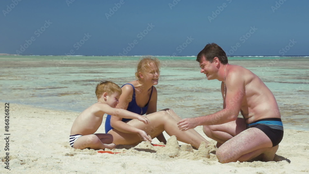 Parents and son playing with sand on the beach Parents and son playing with sand on the beach
