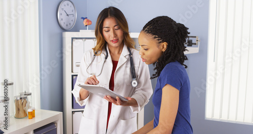 Tela African American patient explaining issues to Asian doctor using tablet