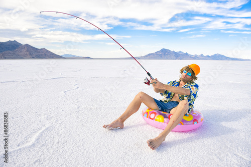 Redneck American fisherman wearing Hawaiian shirt goes on cheap ice fishing vacation holiday with inflatable pink ring in white desert