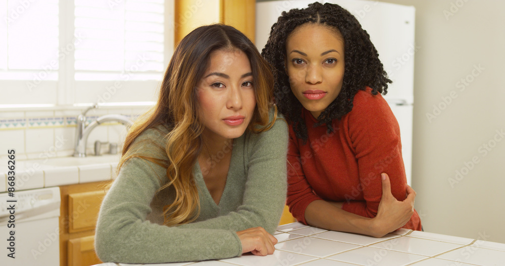 Two women leaning against kitchen counter looking at camera Two women leaning against kitchen counter looking at camera